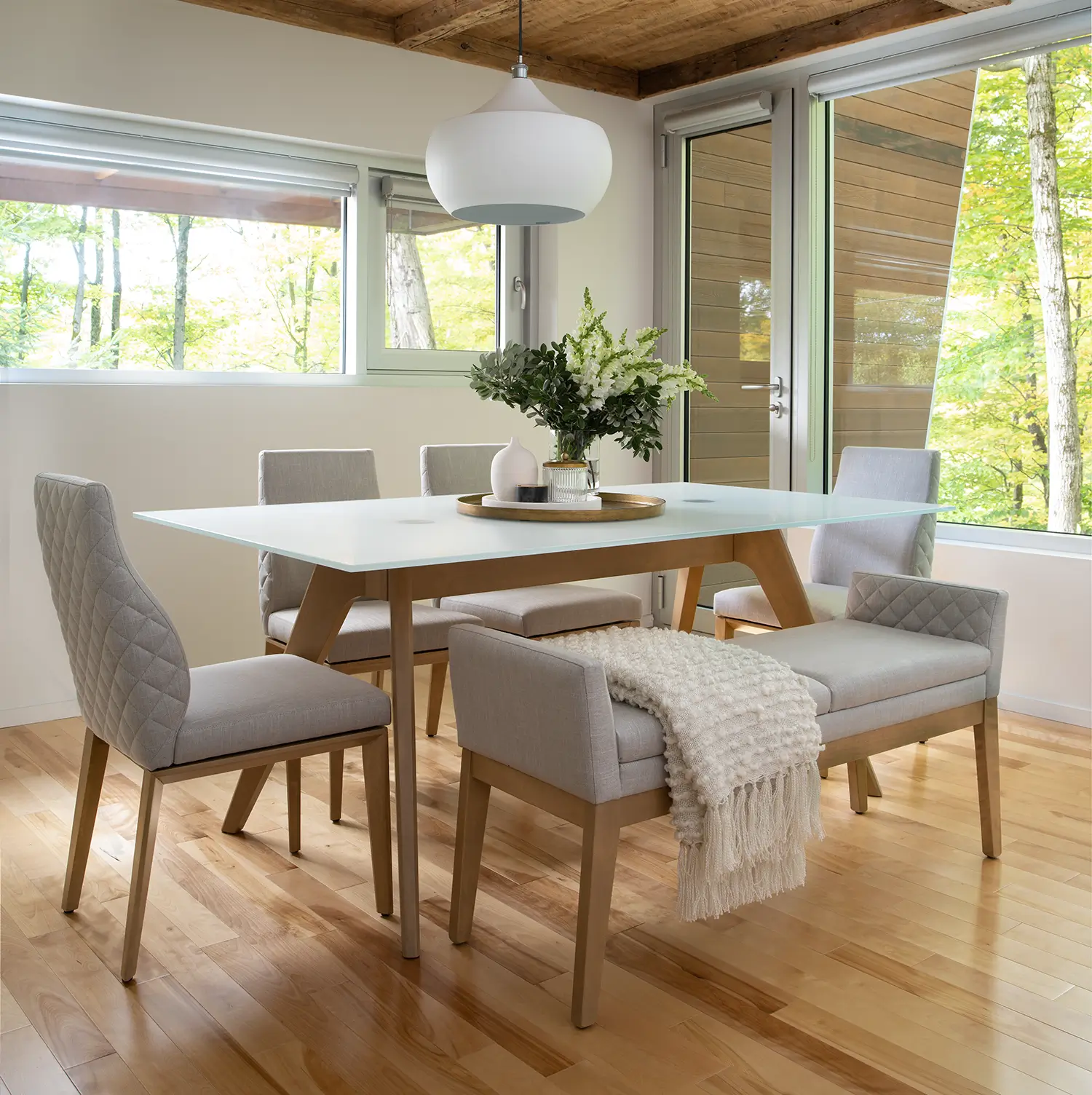 Downtown collection dining table with upholstered chairs and a bench in a sunlit room
