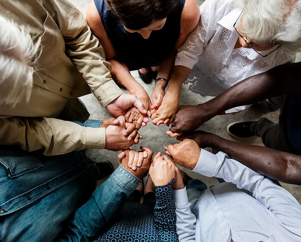A group of people holding hands together in a circle, representing community and support