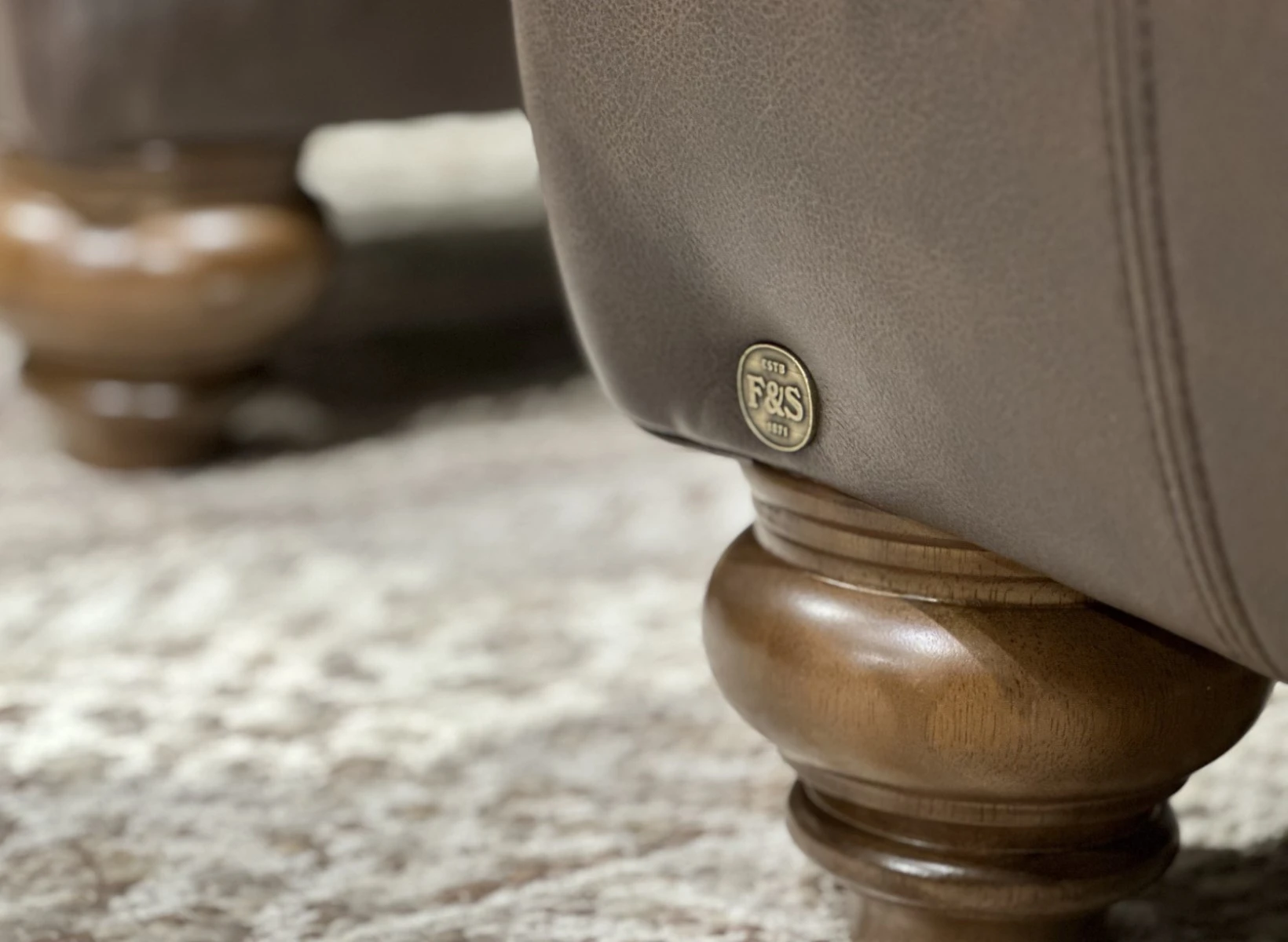 Close-up of a turned wood leg and Field & Stream medallion on a leather sofa