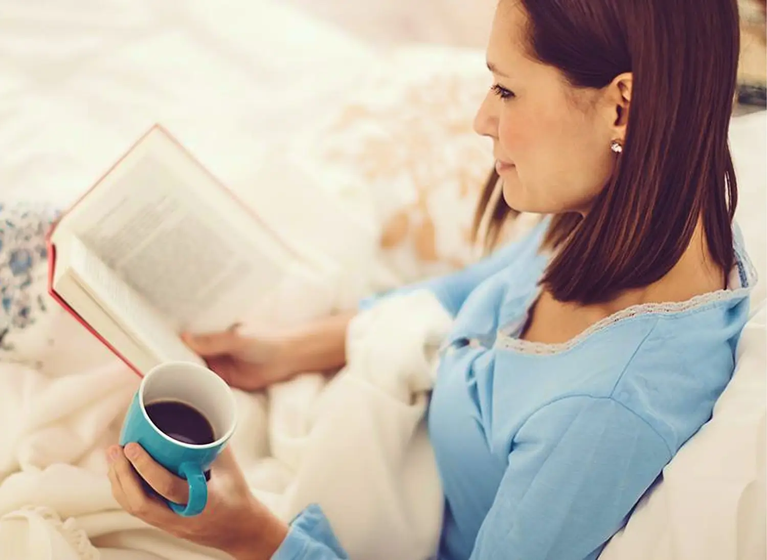 Woman reading and drinking coffee in bed