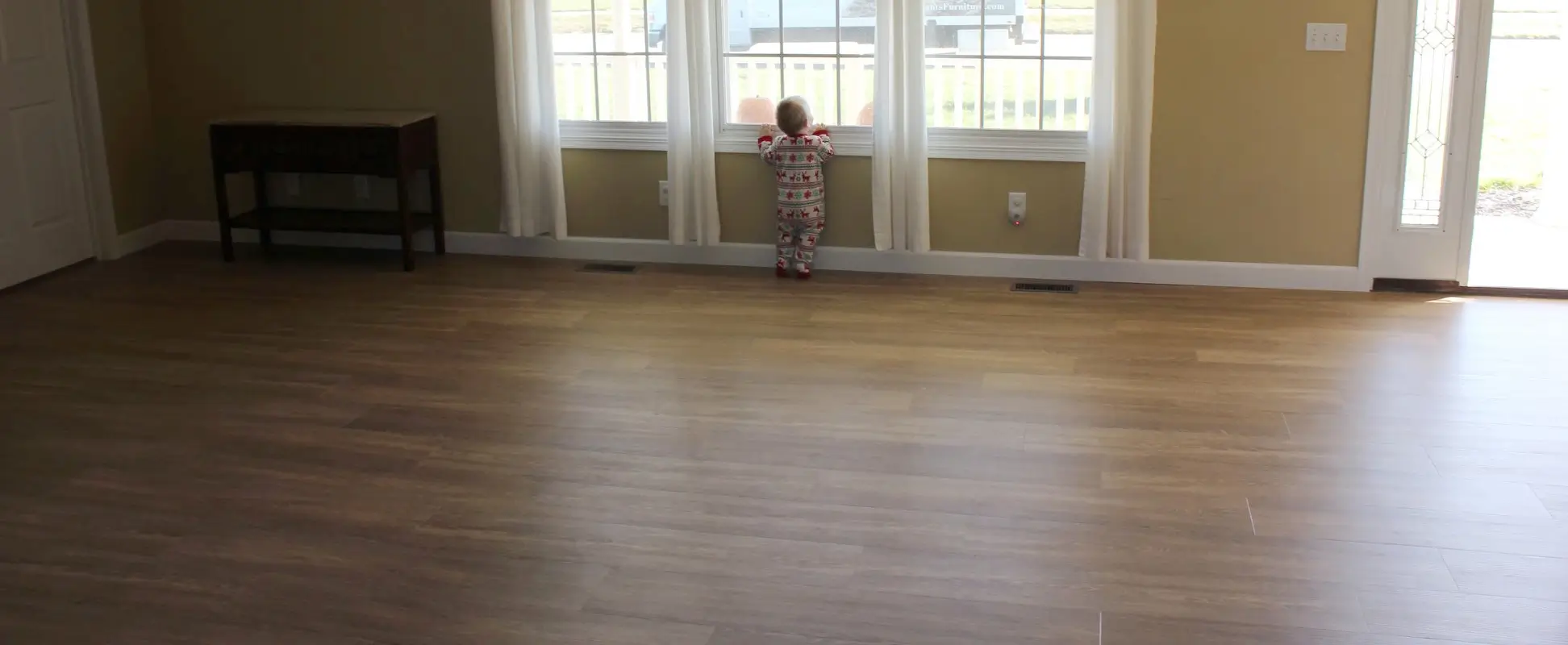 Child standing on hardwood floor looking out the window